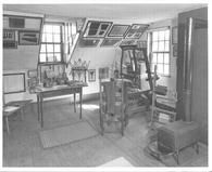 SA0525 - Exhibit at the Fruitlands Museum, Harvard, Mass, showing No. 5 Shaker House, sisters' industries' room, a small loom, stove, yarn winders, table, and chair. Identified on the back., Winterthur Shaker Photograph and Post Card Collection 1851 to 1921c